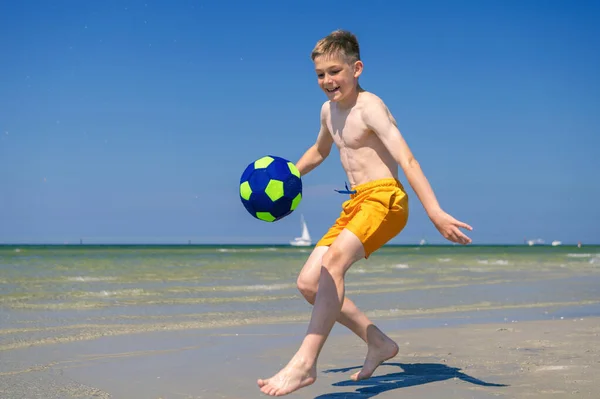 幸せなティーン男の子遊びますとともにボールオンビーチで夏晴れ日とともに青空上の背景 — ストック写真