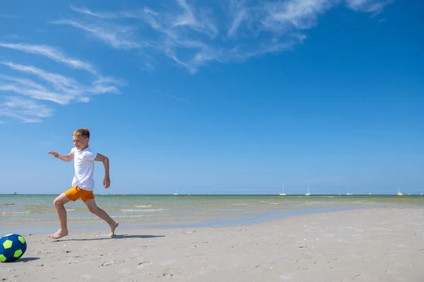 幸せなティーン男の子遊びますとともにボールオンビーチで夏晴れ日とともに青空上の背景 — ストック写真