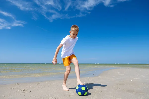 幸せなティーン男の子遊びますとともにボールオンビーチで夏晴れ日とともに青空上の背景 — ストック写真