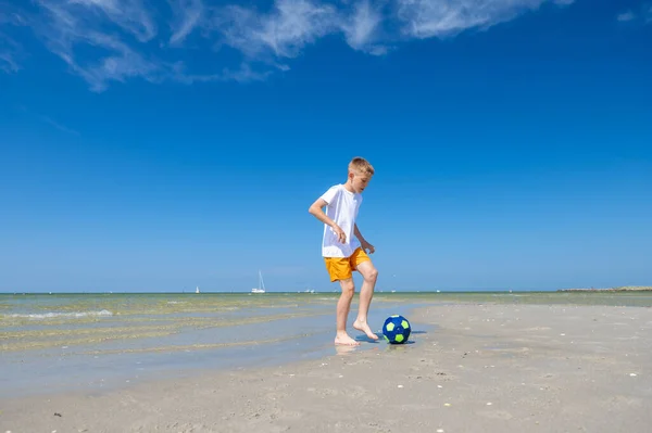 幸せなティーン男の子遊びますとともにボールオンビーチで夏晴れ日とともに青空上の背景 — ストック写真