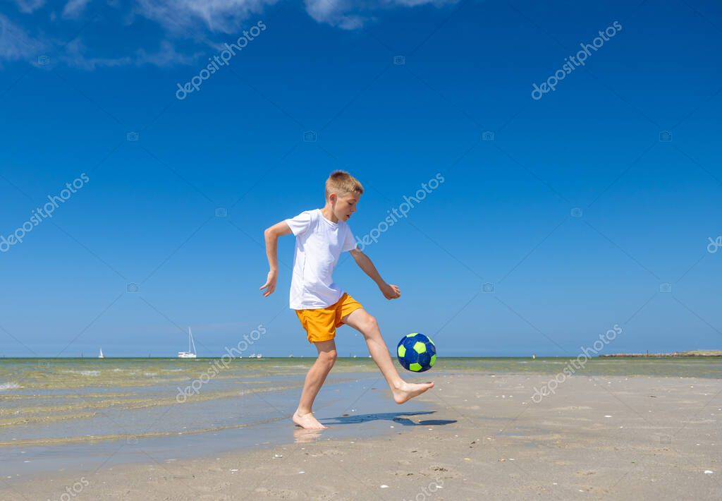 Happy teen boy playing with ball on beach at summer sunny day with blue sky on background