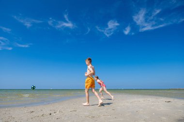 Mutlu çocuklar yaz güneşli bir günde kumsalda top oynuyorlar. Arka planda mavi gökyüzü.