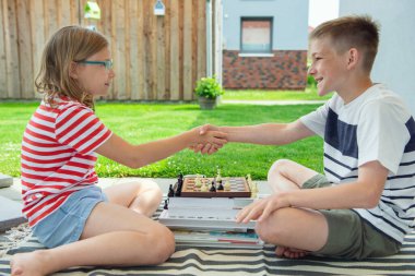 Güneşli bir günde arka bahçede satranç oynayan iki mutlu çocuk yaz tatilinde