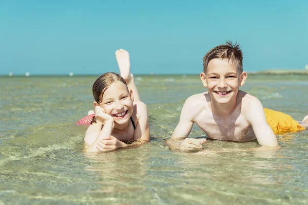 两个快乐的弟妹在夏日的海滩上躺在海水中的画像 — 图库照片