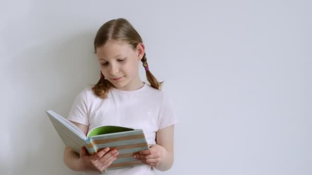 可爱的少女专心致志地阅读关于白墙背景的有趣书籍 — 图库视频影像