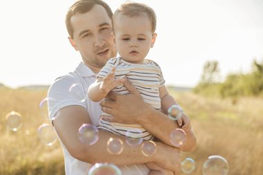 Mutlu, genç, yakışıklı baba yaz günü gün ışığında bebeğini kucağına alıp kucaklıyor.