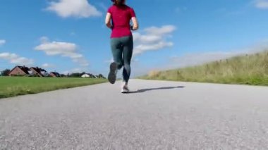 60 fps 4K video, güneşli yaz günlerinde spor kıyafetleriyle koşan güzel bir genç kadın.