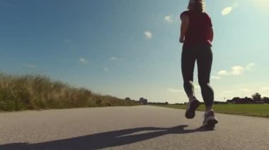 Yavaş çekim 4K video, güneşli bir günde spor giysileriyle koşan genç güzel bir kadın.