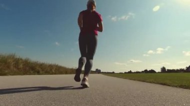 Yavaş çekim 4K video, güneşli bir günde spor giysileriyle koşan genç güzel bir kadın.