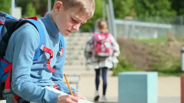 Okul Çocuğu Okul Bahçesinde Oturup Alıştırma Kitabı Yazıyor Ders Bekliyor — Stok video