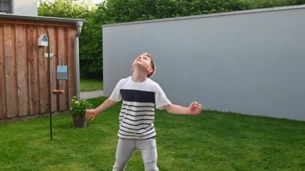 幸せな男の子の4Kビデオ練習彼のフェイントとトリック競争とともにボールで裏庭で自宅で夏休み中 — ストック動画