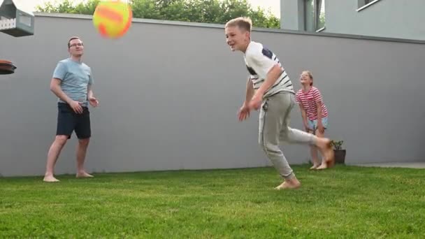 幸せな若い父親は 晴れた夏の日に緑の芝生の上の裏庭で彼の未成年の子供たちとバレーボールをします 60Fpsビデオ — ストック動画