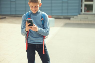 Dersten sonra okul önünde cep telefonuyla sırt çantalı yakışıklı genç çocuk.