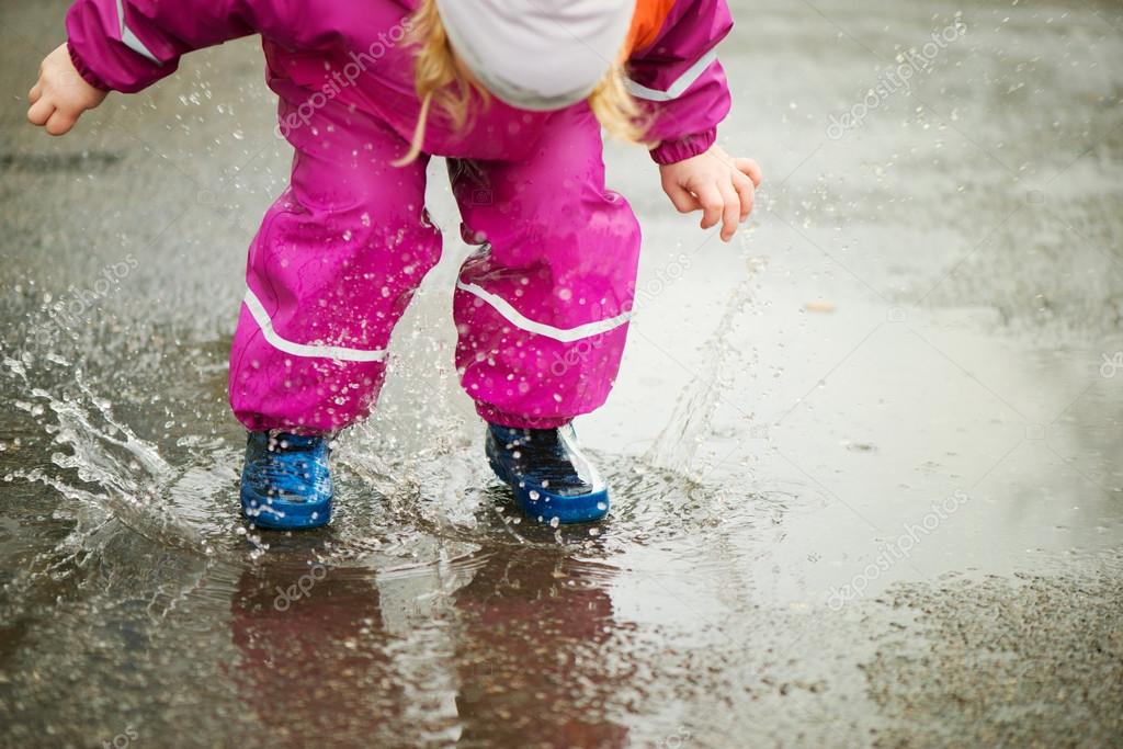 Little happy girl jumping in puddle - Stock Photo, Image. 