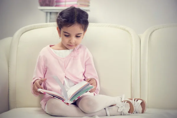 Gadis kecil hispanik lucu membaca buku di sofa — Stok Foto