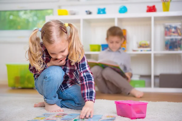Niedliche kleine Mädchen spielen Spiel, Junge lesen Buch lizenzfreie Stockbilder