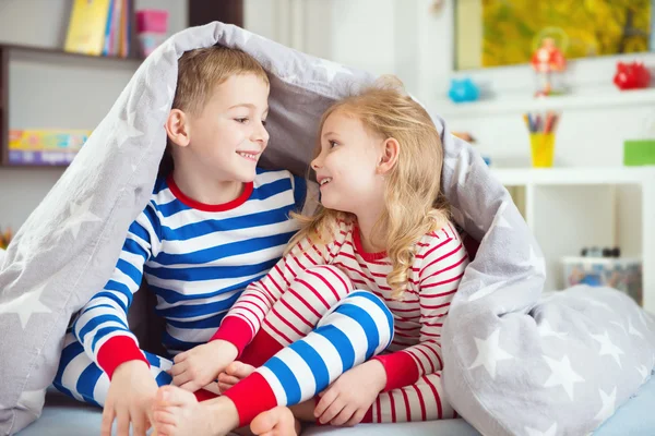 Duas crianças felizes escondidas sob cobertor — Fotografia de Stock