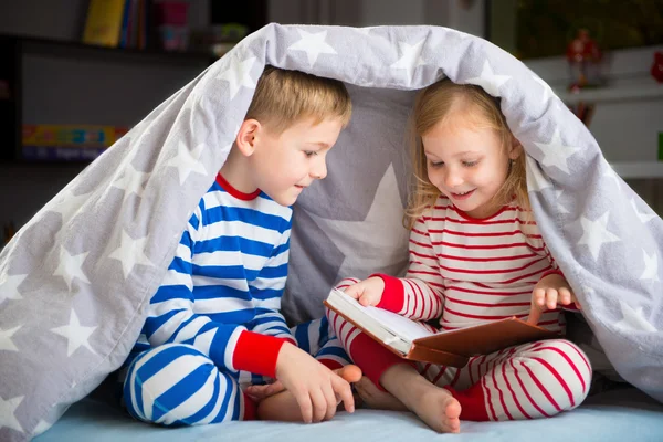 Irmãos felizes lendo livro sob capa — Fotografia de Stock