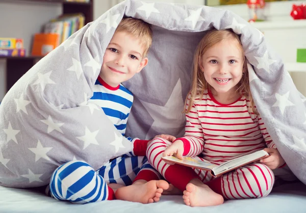 Felices hermanos leyendo libro bajo cubierta — Foto de Stock