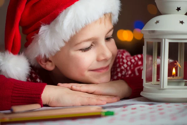 Рождественский ребенок пишет письмо Санте в красной шляпе — стоковое фото