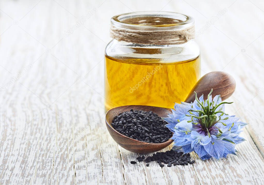 Black cumin oil with flower nigella sativa on white wooden board