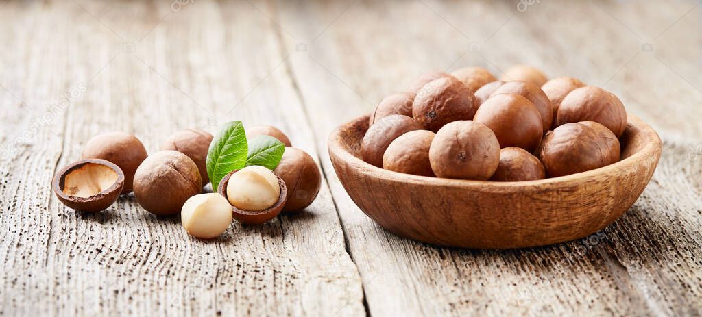 Macadamia nuts with leaves on wooden background