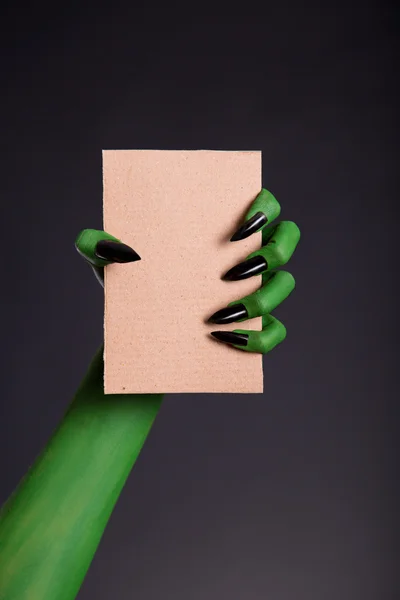 Main de peau verte avec des ongles pointus tenant morceau vide de cardsanglier — Photo