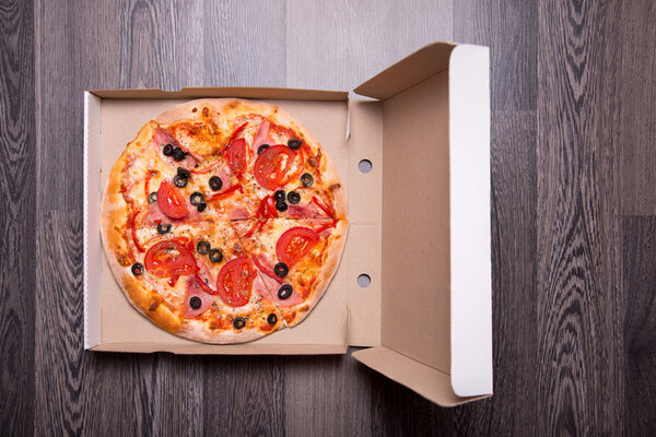 Итальянская пицца с ветчиной, помидорами и оливками в коробке
