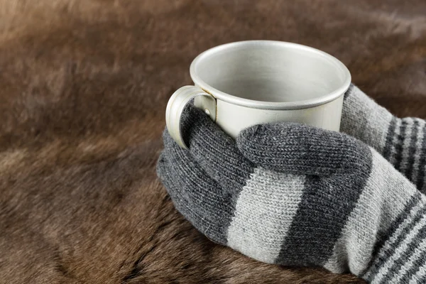 Hands in knitted gloves keep mug