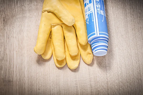 Safety gloves rolled blue construction drawings on wooden board