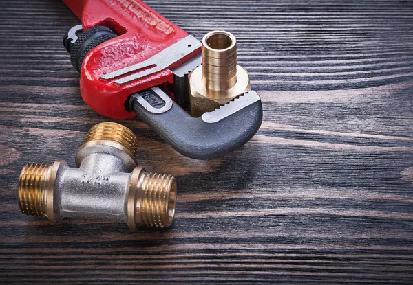 Metal pipe wrench brass equal tee hose nipple on wooden board — Stock Photo, Image