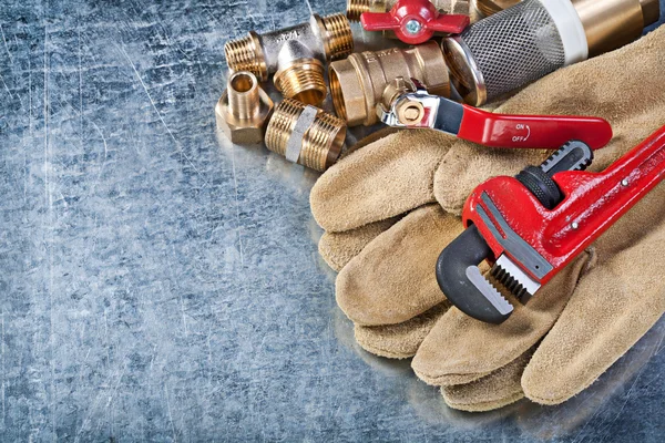 Assortment of plumbing brass hardware safety gloves on metallic — Stock Photo, Image