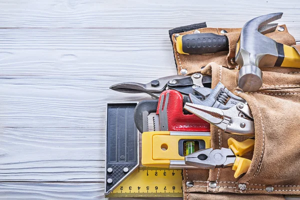 Building implements in leather tool belt on wooden board constru