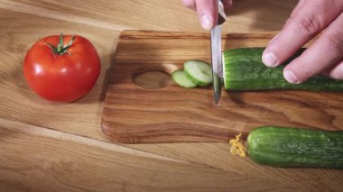 Ahşap doğrama tahtasının üzerinde mutfak bıçağıyla taze yeşil boynuzluyu kesiyor.