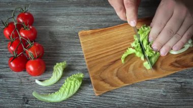 Erkek elleri tahta kesme tahtasında taze yeşil salata yaprakları kesiyor.
