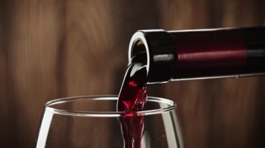 - Şarap. Şarap kadehiyle şarap şişesinden dökülen kırmızı şarap eski ahşap arka planda çok yavaş çekimde.