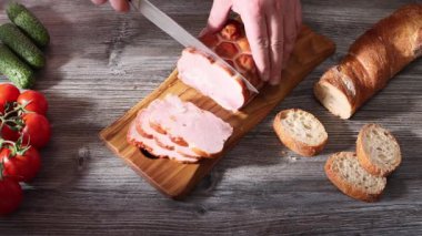 Tahta kesme tahtasının üzerinde somun jambonu dilimliyorum.