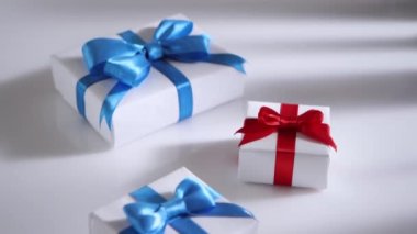 Dolly vurdu. Kamera yavaşça kırmızı ve mavi kurdeleli beyaz hediye kutularının üzerinden geçiyor. Tatil kavramı.