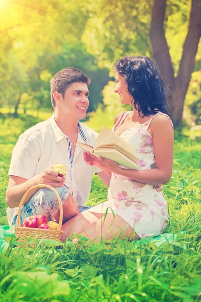 Šťastný mladý pár sedící v trávě, usmíval se a mluví — Stock fotografie
