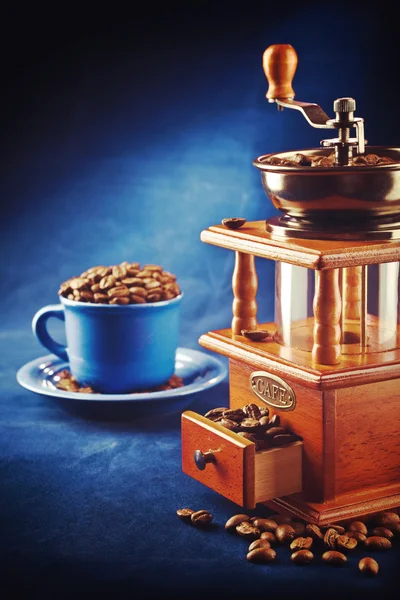 Coffee grinder with beans and cup on saucer standing on blue tab — Stock Photo, Image