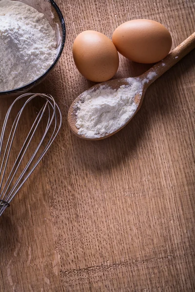 Eggs, flour, corolla on wooden board — Stock Photo, Image