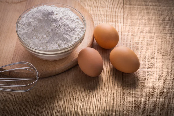 Three eggs and bowl with flour — Stock Photo, Image