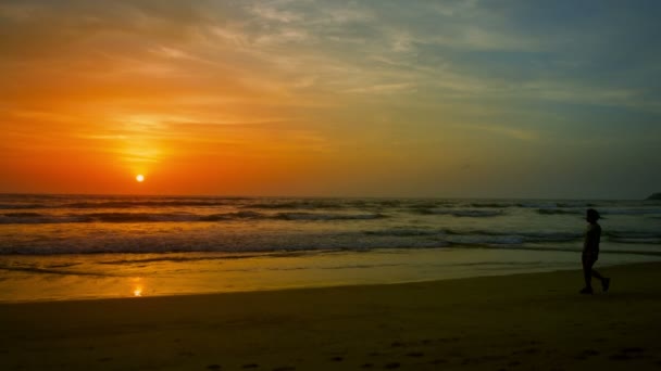 熱帯のビーチに沈む夕日。女性は、水の端に沿って歩く — ストック動画