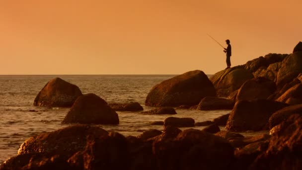 KAMALA. PHUKET. TAILANDIA - CIRCA DIC 2014: Silueta de pescador. pescar desde las rocas al atardecer. con mar abierto y horizonte en el fondo . — Vídeos de Stock