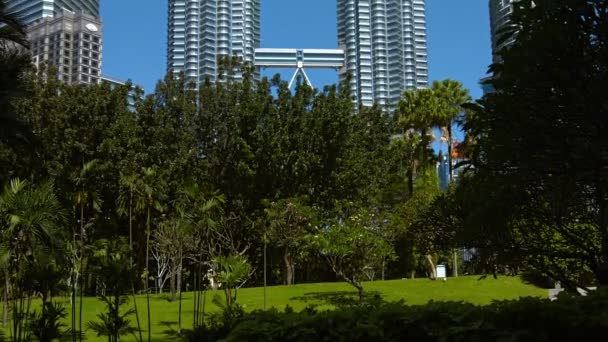 Tiro inclinado para cima das famosas Torres Gêmeas Petronas. chegando ao céu azul claro. como visto de Kuala Lumpur City Centre Park na capital da Malásia . — Vídeo de Stock