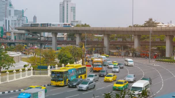 在曼谷市中心的一个巨大的回旋处的典型城市交通。与高架通勤列车在后台 — 图库视频影像