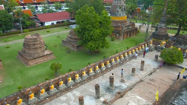 Ayutthaya. Thailand-circa feb 2015: rad av identiska Buddha skulpturer längs en sönderfallande tegelvägg med gamla stupas i bakgrunden på Wat Yai Chai Mongkhon i Ayutthaya Thailand. — Stockvideo