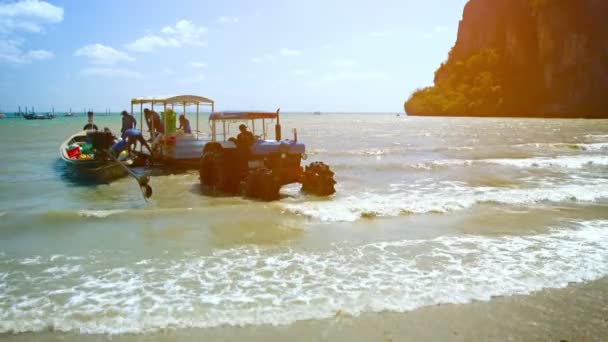 Arbeiter laden Fracht und Vorräte von einem Boot in den Untiefen ab. auf einem Anhänger. von einem Traktor auf einen Strand in Thailand gezogen werden. — Stockvideo