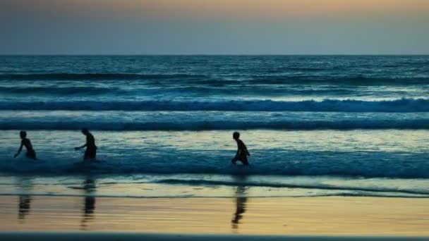 Video fullhd - Teenager spielen mit einem Ball in den Wellen des tropischen Meeres bei Sonnenuntergang — Stockvideo