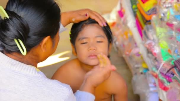 BAGAN, MYANMAR - CIRCA JAN 2014: Mother applies sunscreen thanaka on her daughter's skin — Stock Video